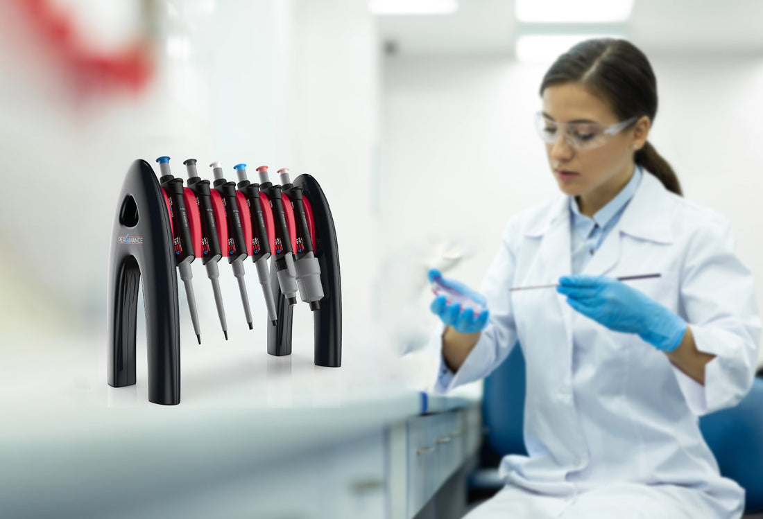 Lab worker handling samples alongside a set of lab pipettes on a stand.